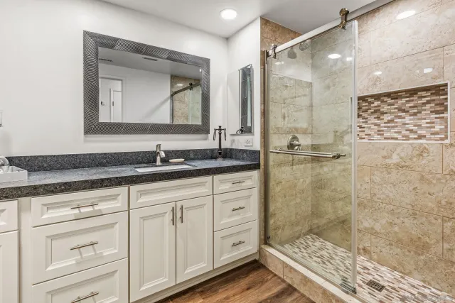 a bathroom with a granite countertop sink a mirror a vanity and shower