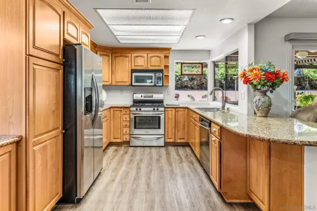 a kitchen with stainless steel appliances granite countertop a refrigerator a sink dishwasher a stove and a dining table with wooden floor