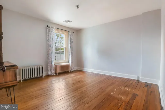 a view of an empty room with wooden floor and a bench