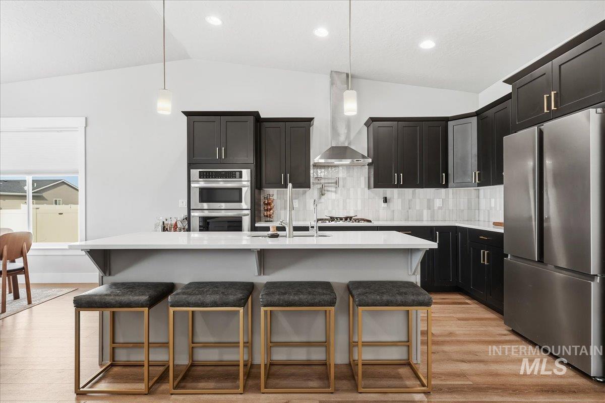 305 Tiffany Rose Way Wilder, ID 83676 - Photo 8 of 31 Kitchen featuring vaulted ceiling, stainless steel appliances, dark cabinets, a kitchen bar, and hanging light fixtures