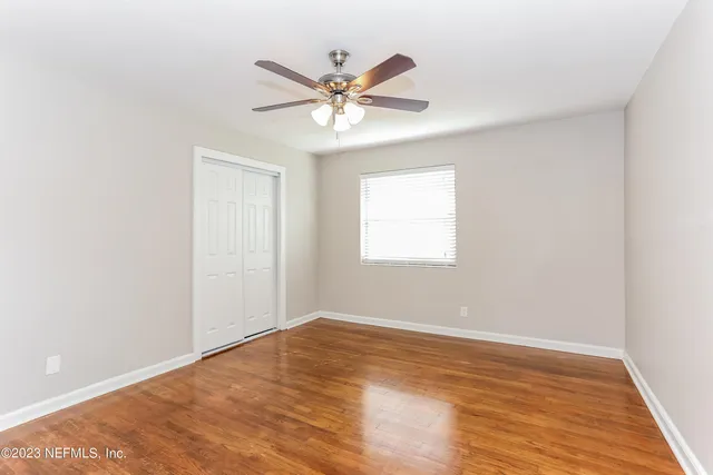 an empty room with wooden floor fan and windows