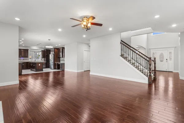 a view of an empty room with wooden floor stairs and a kitchen view