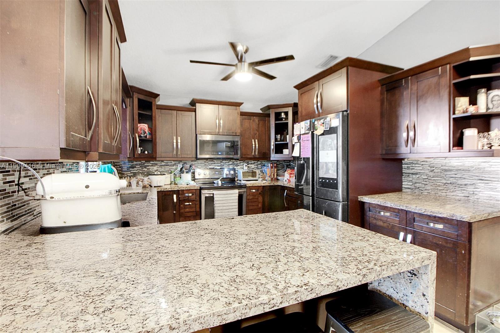 14880 Southwest 56th Terrace Miami, FL 33193 - Photo 14 of 35 a kitchen with stainless steel appliances kitchen island granite countertop wooden cabinets a refrigerator sink and stove