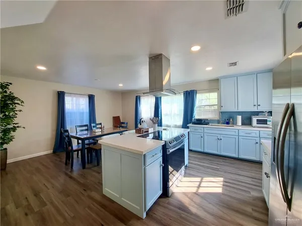 a kitchen with stainless steel appliances kitchen island granite countertop a stove a sink a refrigerator and white cabinets with wooden floor