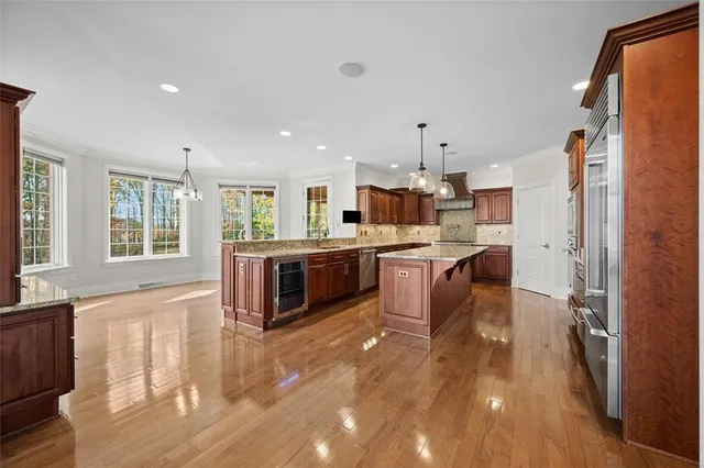 a kitchen with stainless steel appliances kitchen island granite countertop a stove a sink a refrigerator and white cabinets with wooden floor