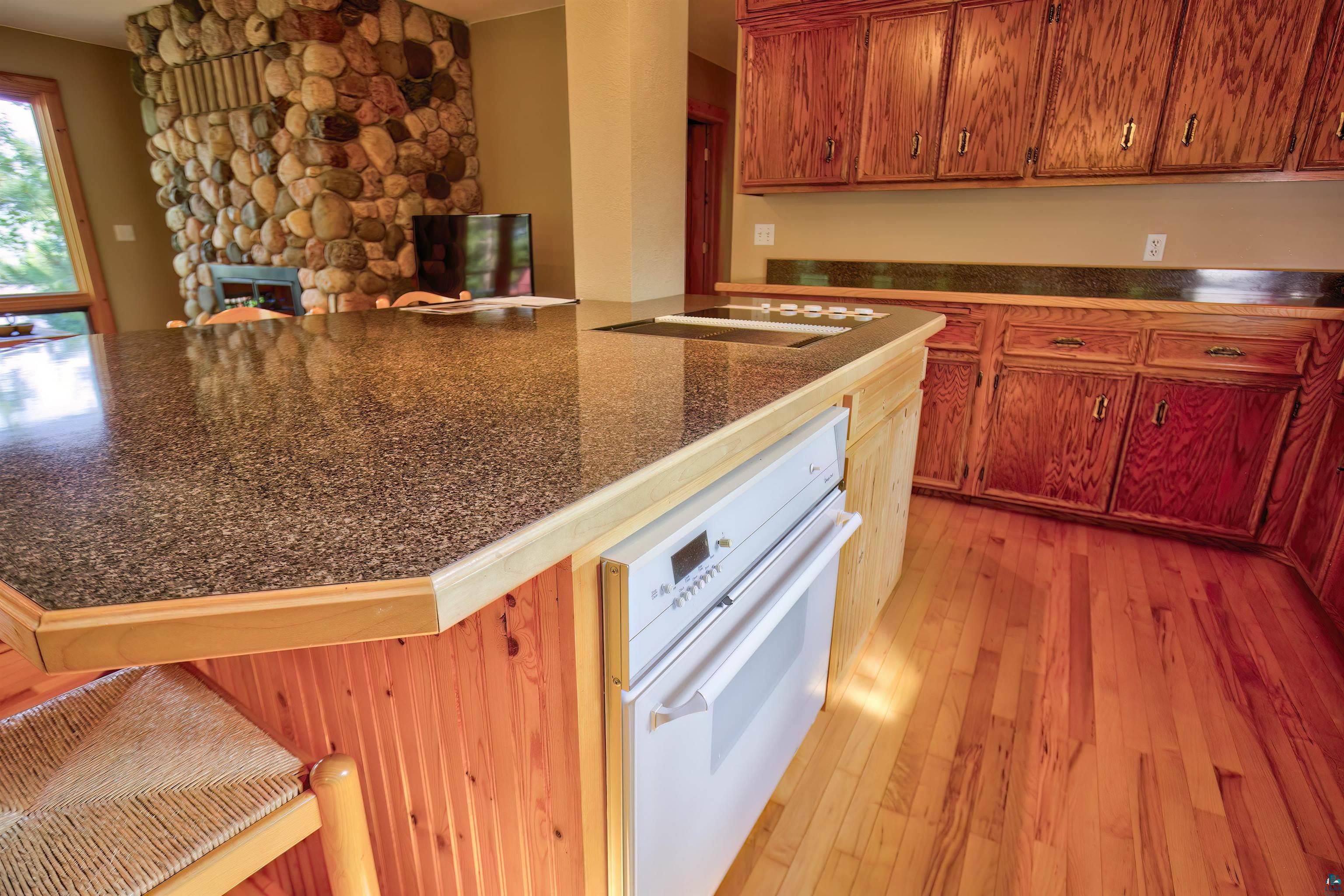 12351 Endless Waters Road Ely, MN 55731 - Photo 24 of 48 Kitchen featuring oven, light wood finished floors, a breakfast bar, a stone fireplace, and dark countertops
