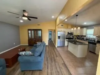 a large open kitchen with stainless steel appliances kitchen island granite countertop a refrigerator a stove a sink and a dining table with wooden floor