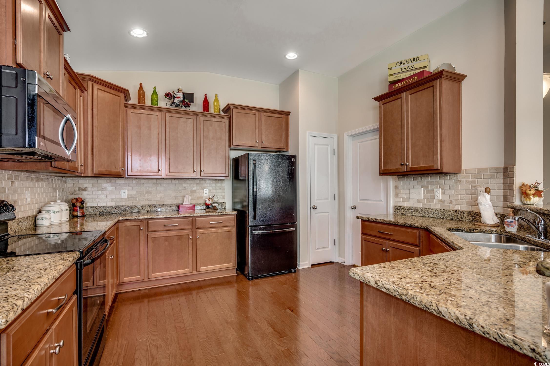 202 Fox Den Drive Murrells Inlet, SC 29576 - Photo 16 of 35 Kitchen featuring black appliances, tasteful backsplash, light stone counters, dark wood-style flooring, and brown cabinets