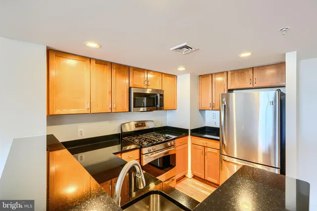 a kitchen with stainless steel appliances granite countertop a refrigerator a stove a sink a dining table and chairs with wooden floor