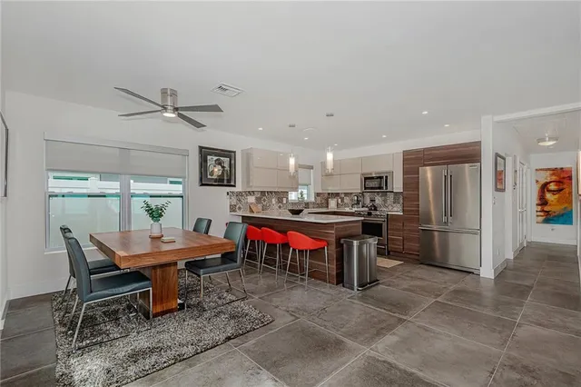 a kitchen with stainless steel appliances kitchen island granite countertop a dining table chairs refrigerator sink and microwave