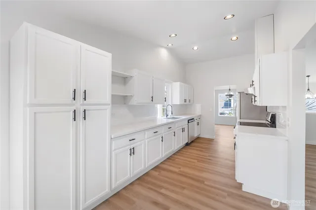 a large white kitchen with wooden floor and stainless steel appliances