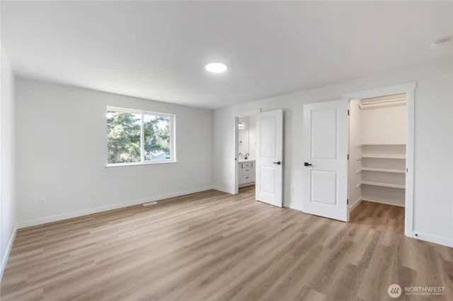 an empty room with wooden floor closet and windows