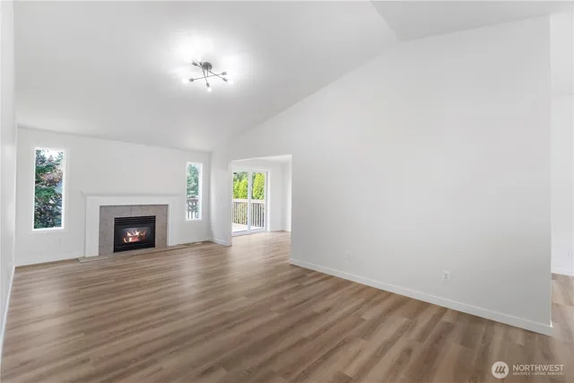 a view of an empty room with wooden floor fireplace and a window