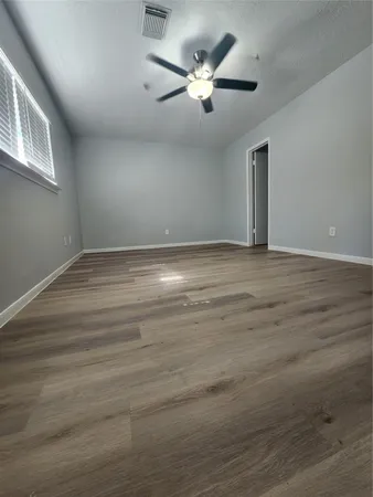 a view of an empty room with chandelier fan and wooden floor