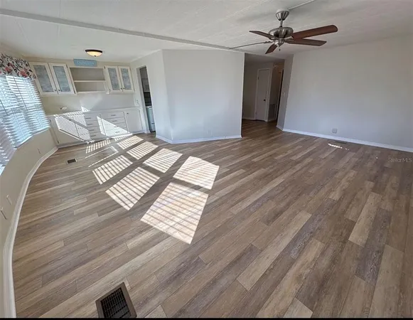 a view of an empty room with wooden floor and a ceiling fan