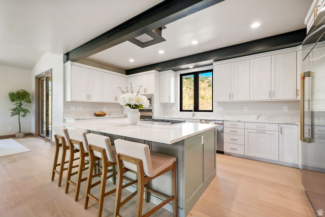 10646 North Reflection Ridge Hideout, UT 84036 - Photo 10 of 43 Bright kitchen featuring a large central island with seating, white shaker cabinetry, stainless steel appliances, and light wood-finish flooring