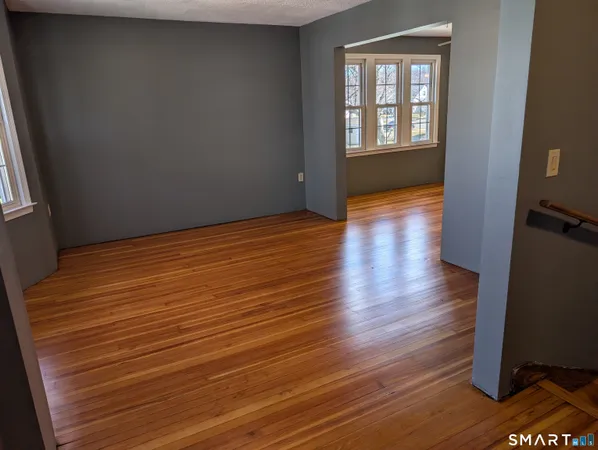 a view of a elevator and an empty room with wooden floor