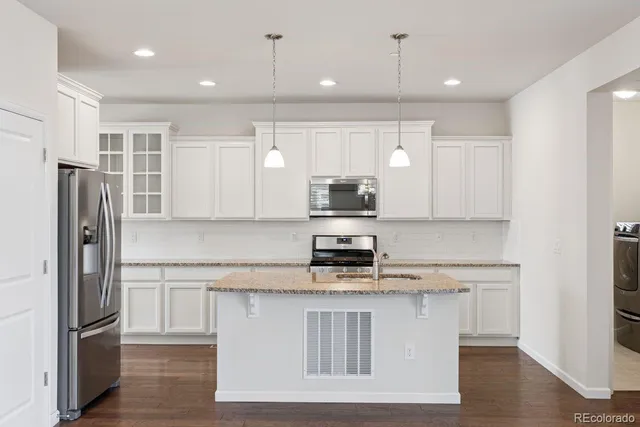 a kitchen with kitchen island granite countertop a refrigerator a sink and white cabinets