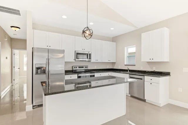 a kitchen with stainless steel appliances granite countertop a sink a stove a refrigerator and white cabinets