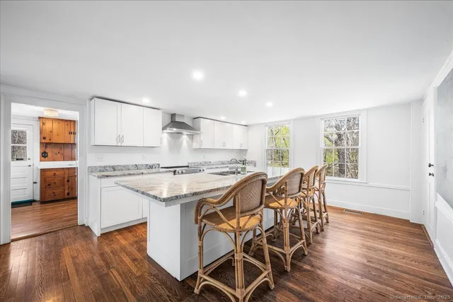 a kitchen with stainless steel appliances granite countertop a stove top oven a sink dishwasher and white cabinets with wooden floor