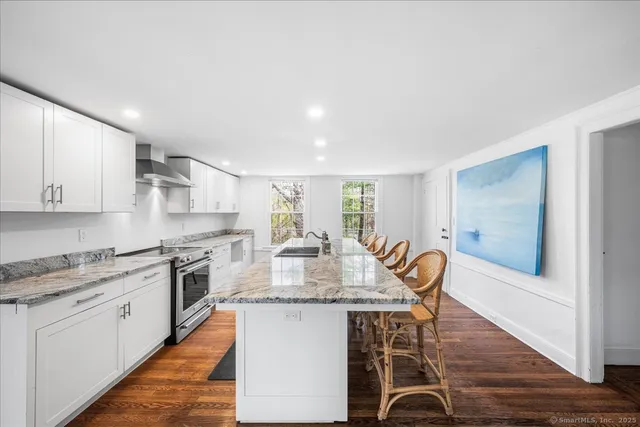 a kitchen with stainless steel appliances granite countertop a stove top oven a sink dishwasher and white cabinets with wooden floor