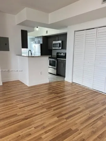a view of kitchen and empty room with wooden floor