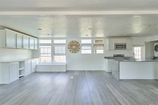 a kitchen with granite countertop a stove a sink and white cabinets with wooden floor next to windows