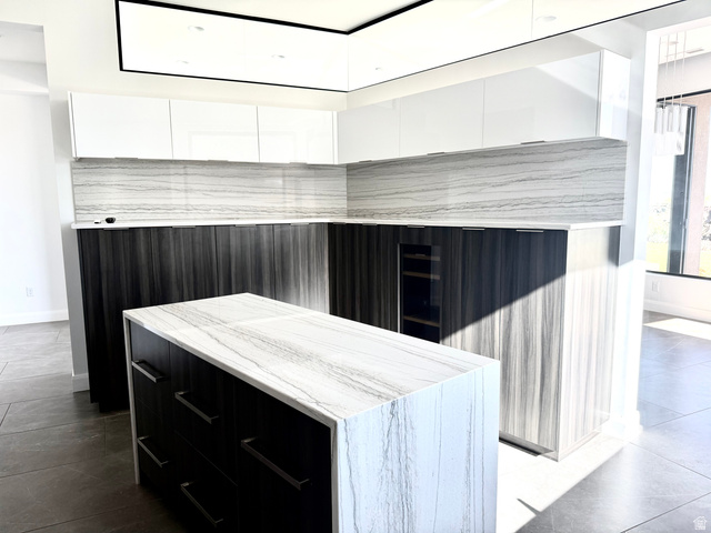 1500 Split Rock, Unit 150 Ivins, UT 84738 - Photo 13 of 18 Contemporary kitchen featuring an island with a waterfall-edge countertop, two-tone cabinetry with white upper and dark wood-finish lower units, full-height stone slab backsplash, and a built-in beverage cooler