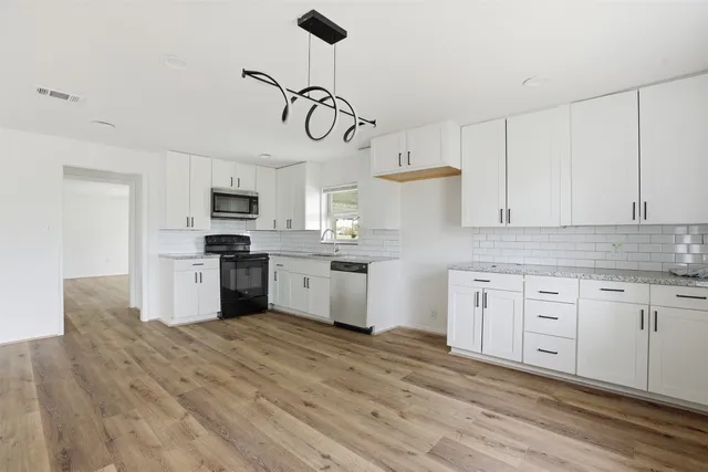 a kitchen with stainless steel appliances granite countertop a stove a sink dishwasher a refrigerator and white cabinets with wooden floor