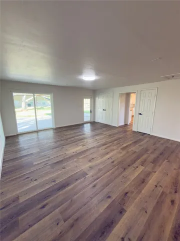 a view of an empty room with wooden floor and window
