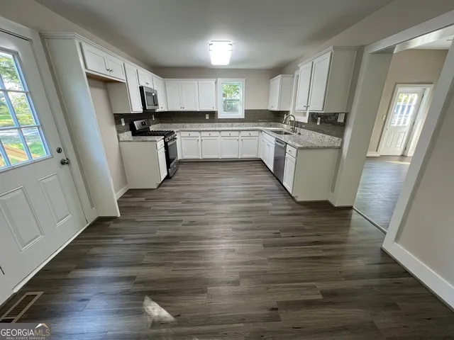 a kitchen with wooden floors white cabinets appliances and a sink