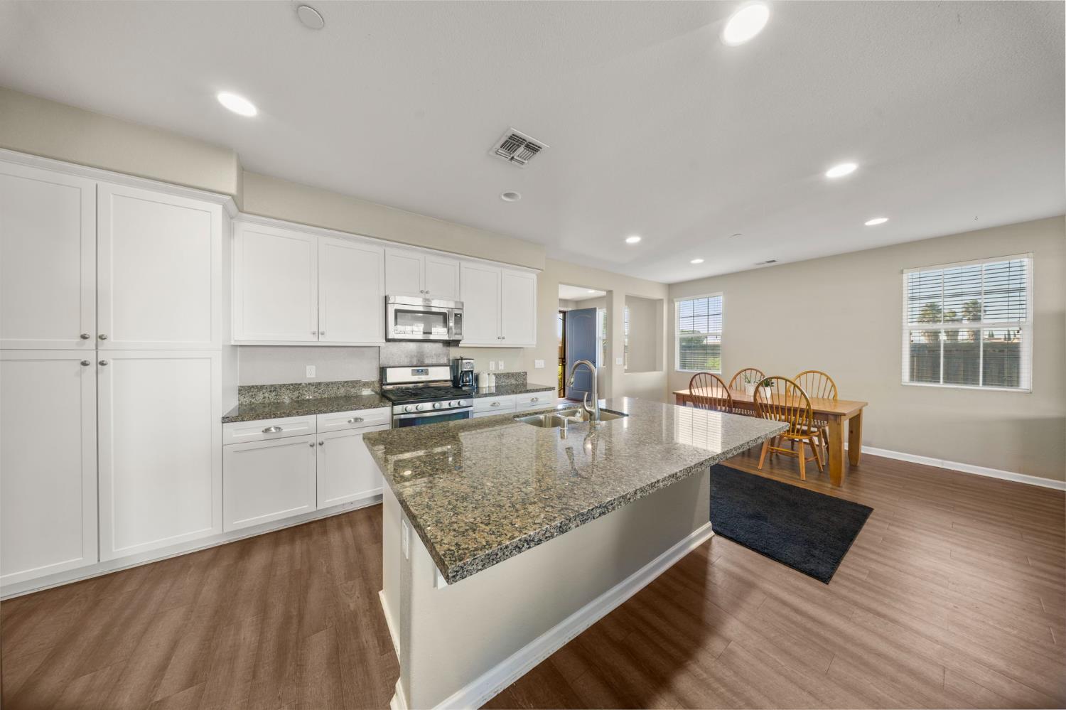 2685 Remy Javier Street Tracy, CA 95377 - Photo 7 of 26 a large kitchen with kitchen island a stove a refrigerator a sink dishwasher with a dining table and chairs with wooden floor