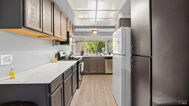 a kitchen with stainless steel appliances granite countertop a refrigerator a sink dishwasher a stove and white countertops with wooden floor