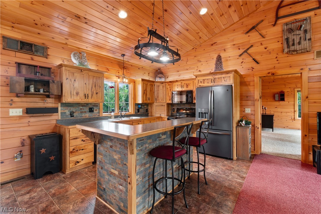 8205 Lake Road Seville, OH 44273 - Photo 11 of 35 Kitchen featuring stone backsplash, Hickory wood cabinets, dark appliances, wooden ceiling, a center island, vinyl tile flooring, lofted ceiling, wooden walls, and a high ceiling