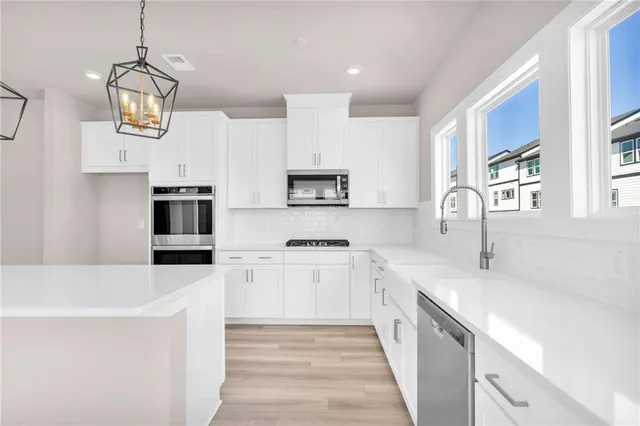 a kitchen with stainless steel appliances a stove top oven a sink a refrigerator white cabinets and wooden floor