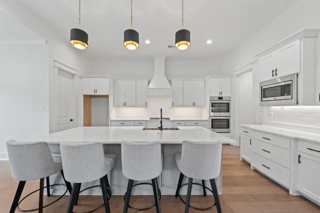 a kitchen with stainless steel appliances kitchen island granite countertop a dining table chairs and white cabinets