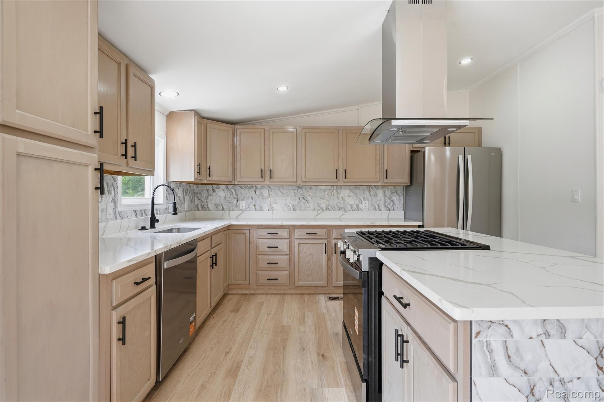 4420 Dublin Road Burton, MI 48529 - Photo 11 of 56 Modern kitchen featuring light wood-finish cabinetry, white countertops with veining, a stainless steel range hood, a kitchen island with a built-in range, and wood-finish flooring