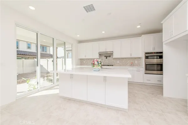 a kitchen with stainless steel appliances a sink a stove a refrigerator with white cabinets and wooden floor