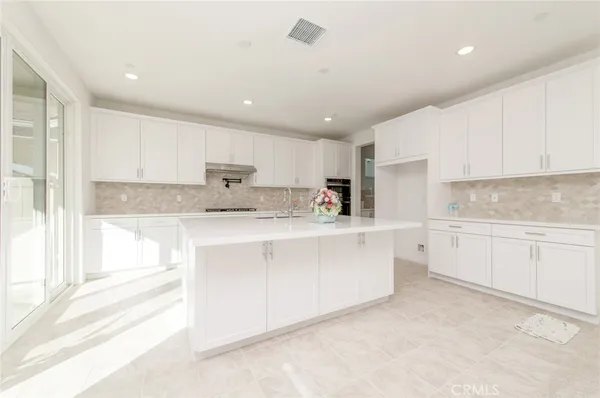 a large white kitchen with kitchen island a sink stainless steel appliances and cabinets