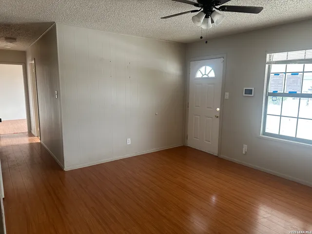 an empty room with wooden floor fan and windows