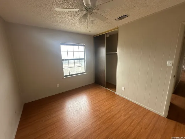 an empty room with wooden floor fan and windows