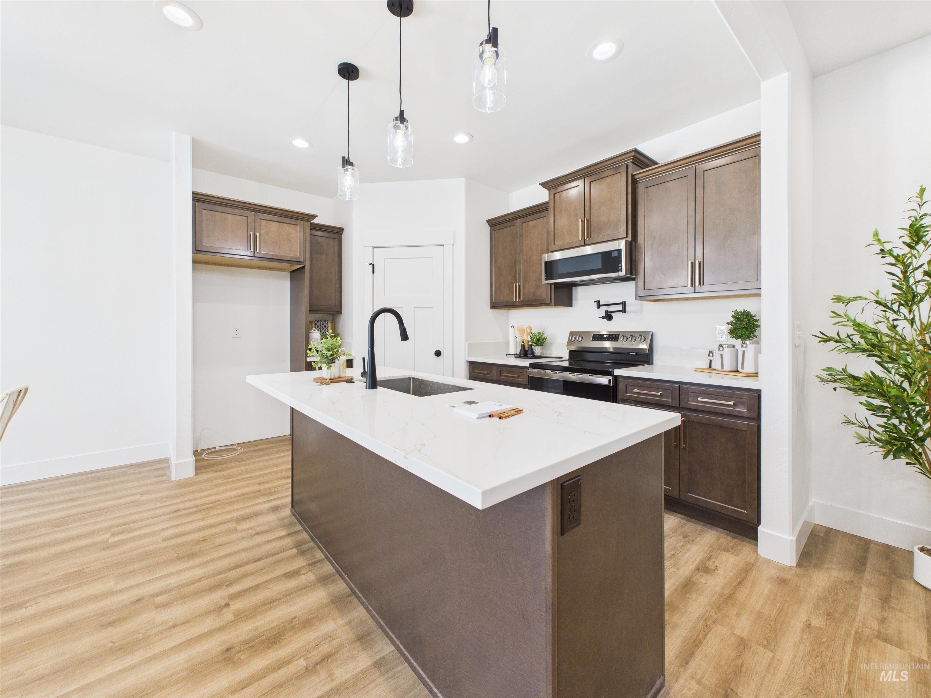 1216 Bronze Drive Rupert, ID 83350 - Photo 8 of 28 Kitchen featuring decorative light fixtures, dark brown cabinets, appliances with stainless steel finishes, an island with sink, and light wood finished floors