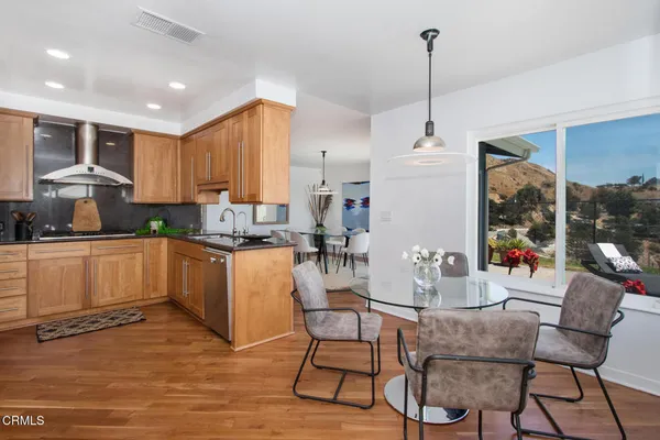a kitchen with stainless steel appliances granite countertop a stove top oven a sink dishwasher a dining table and chairs with wooden floor