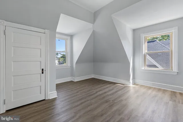 an empty room with wooden floor staircase and windows