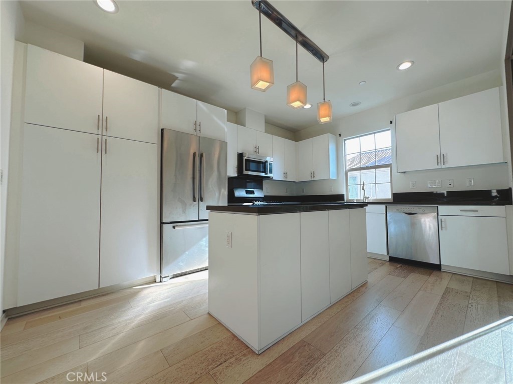 87 Evening Sun Irvine, CA 92620 - Photo 8 of 20 a kitchen with kitchen island granite countertop a refrigerator a sink dishwasher a stove and white cabinets with wooden floor
