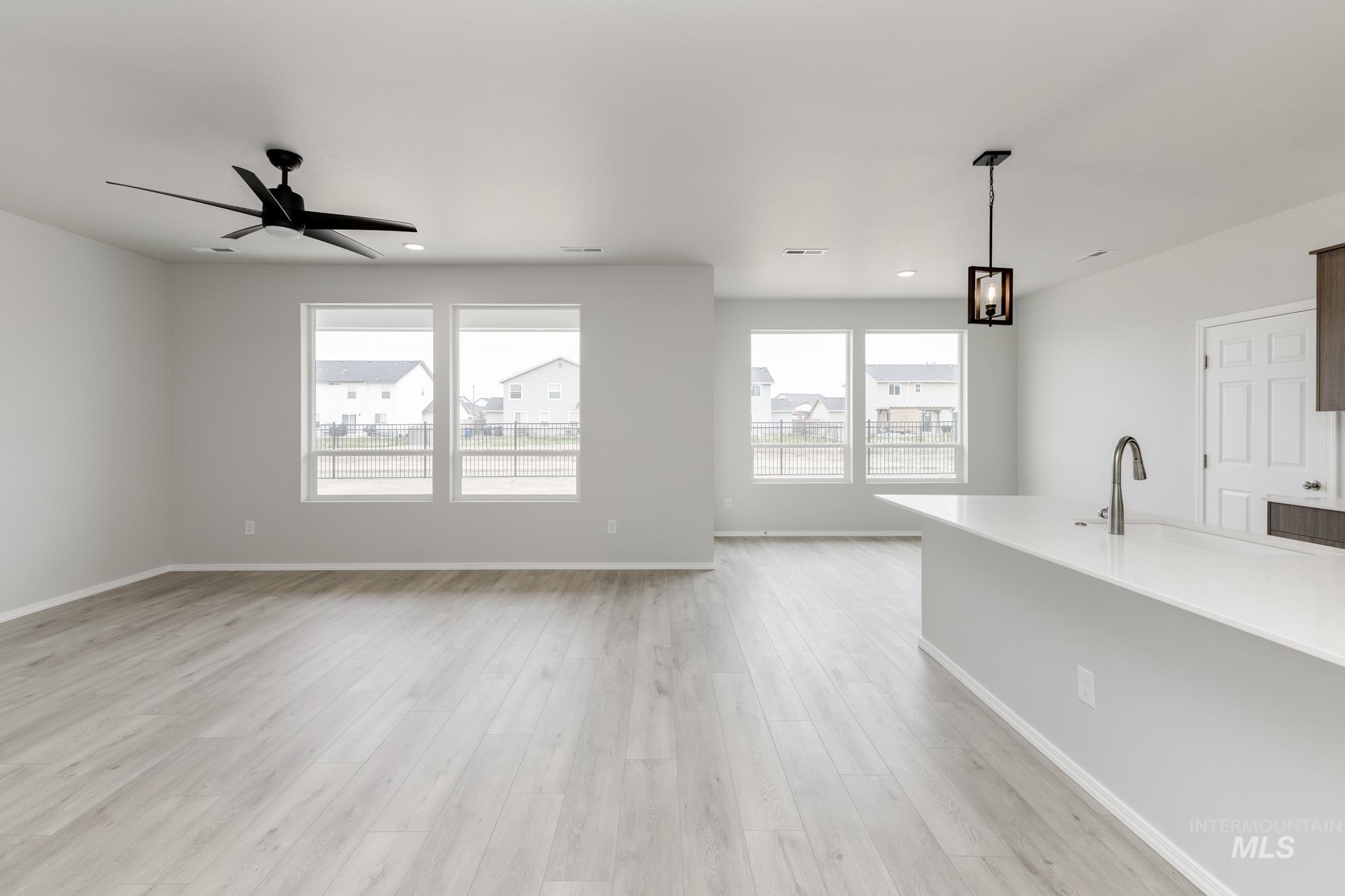 12842 Ropers Street Nampa, ID 83651 - Photo 8 of 29 Spacious room featuring light wood-finish flooring, multiple large windows, a sleek black ceiling fan, and a kitchen island with a built-in sink and pendant light fixture