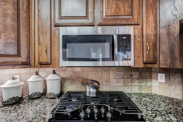 a kitchen with stainless steel appliances granite countertop wooden cabinets a sink a stove a refrigerator and island