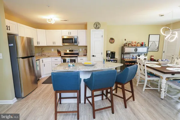 a kitchen with stainless steel appliances granite countertop a dining table chairs refrigerator and sink