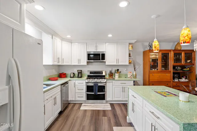 a kitchen with stainless steel appliances granite countertop a stove top oven a sink dishwasher and a refrigerator with wooden floor