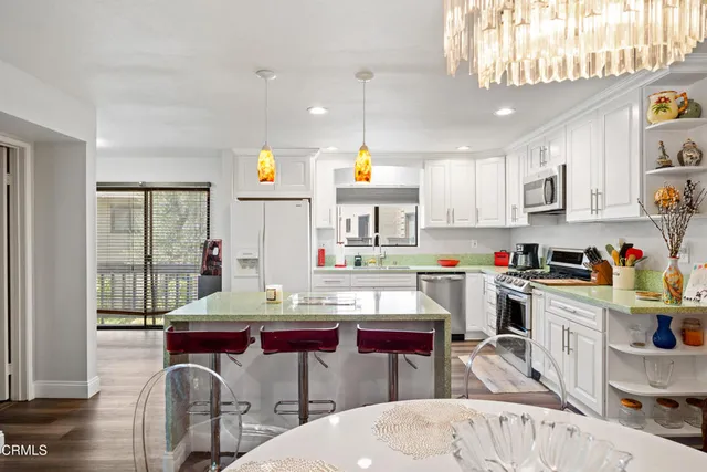 a kitchen with stainless steel appliances kitchen island granite countertop a dining table chairs sink and cabinets